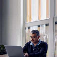 side view of a man sitting at the kitchen table with his laptop and paperwork